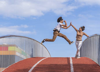 Man jumping mid air on bridge, highfiving woman - DLTSF00560