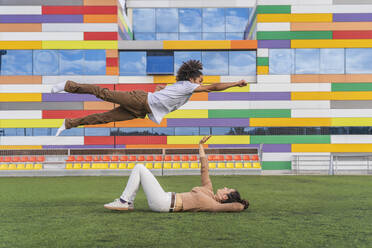 Dancer jumping super hero style over partner, lying on grass - DLTSF00563