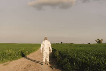 Man wearing protective suit and mask in the countryside - ERRF02631