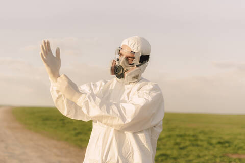 Mann mit Schutzanzug und Maske auf dem Lande, der Schutzhandschuhe anzieht, lizenzfreies Stockfoto