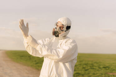 Mann mit Schutzanzug und Maske auf dem Lande, der Schutzhandschuhe anzieht - ERRF02642