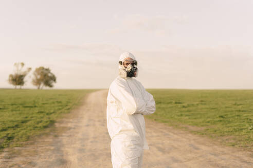 Portrait of man wearing protective suit and mask standing on dirt track in the countryside - ERRF02644