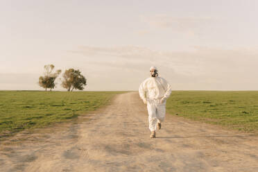 Man wearing protective suit and mask running on dirt track in the countryside - ERRF02645