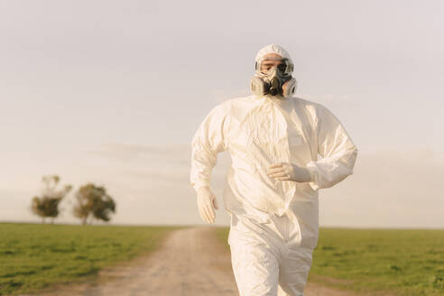 Man wearing protective suit and mask running in the countryside - ERRF02646