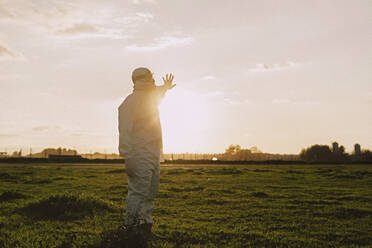 Man wearing protective suit and mask in the countryside at sunset - ERRF02647