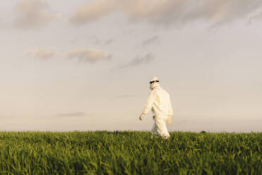 Rear view of man wearing protective suit walking in the countryside - ERRF02648