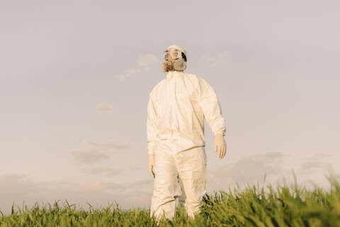 Mann mit Schutzanzug und Maske in einem Feld, lizenzfreies Stockfoto