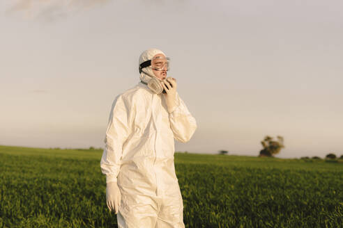 Man wearing protective suit in the countryside taking off respirator - ERRF02656