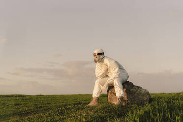 Mann mit Schutzanzug und Maske sitzt auf einem Felsen in der Landschaft - ERRF02660