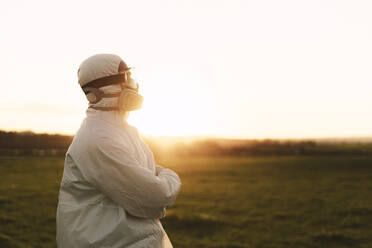Man wearing protective suit and mask in the countryside at sunset - ERRF02672