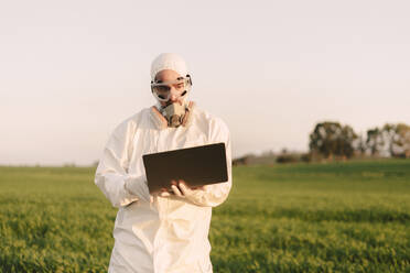 Mann mit Schutzanzug und Maske auf dem Lande, der einen Laptop benutzt - ERRF02675