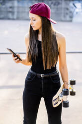 Junge Frau mit Smartphone und Skateboard im Skatepark - GIOF08022