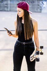 Young woman with smartphone and skateboard at skatepark - GIOF08022