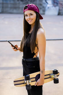 Junge Frau mit Smartphone und Skateboard im Skatepark - GIOF08024