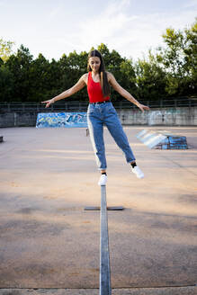 Junge Frau balanciert auf einer Schiene im Skatepark - GIOF08026