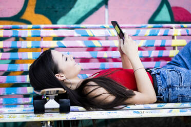 Junge Frau liegt auf einer Bank im Skatepark - GIOF08031