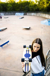 Porträt einer jungen Frau mit Skateboard im Skatepark - GIOF08035