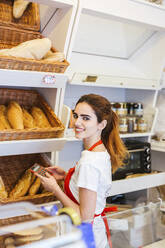 Junge Frau arbeitet in einer Bäckerei und benutzt einen Taschenrechner - LJF01327