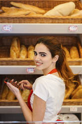 Junge Frau arbeitet in einer Bäckerei und benutzt einen Taschenrechner - LJF01344