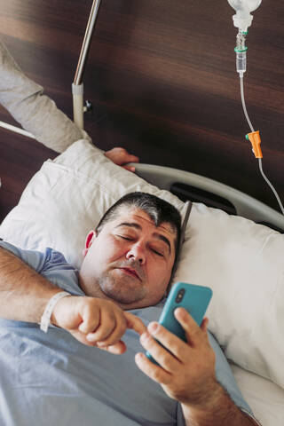 Patientin liegt im Krankenhausbett und benutzt ein Mobiltelefon, lizenzfreies Stockfoto