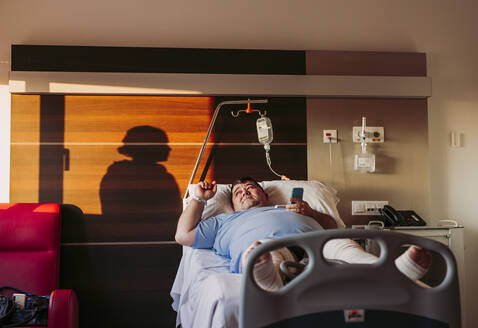 Patient lying in hospital bed with silhouette of a woman behind curtain - LJF01351