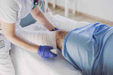 Nurse wrapping bandage around patient's leg in hospital bed - LJF01353