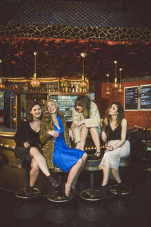 Vier glückliche Frauen sitzen an der Bar in einem Club - HBIF00045