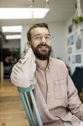 Young man sitting on chair, looking at camera, smiling - PESF01805