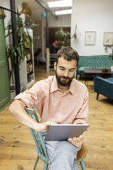 Young man sitting on chair, using digital tablet - PESF01807