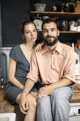 Junges Paar sitzt lächelnd auf der Küchenarbeitsplatte - PESF01810