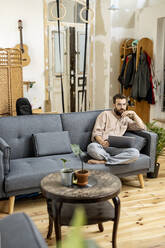 Junger Mann sitzt zu Hause auf der Couch und benutzt ein digitales Tablet - PESF01815