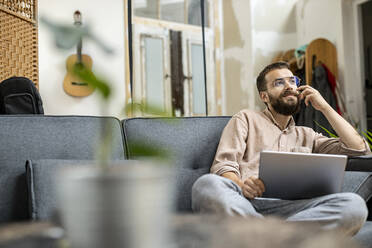 Junger Mann sitzt zu Hause auf der Couch und benutzt ein digitales Tablet - PESF01818