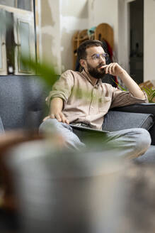 Junger Mann sitzt zu Hause auf der Couch und benutzt ein digitales Tablet - PESF01819