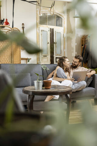 Junges Paar sitzt zu Hause auf der Couch und benutzt ein digitales Tablet, lizenzfreies Stockfoto