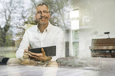 Älterer Mann mit grauen Haaren in modernem Design Wohnzimmer mit Tablet sitzen auf Couch - SBOF02085