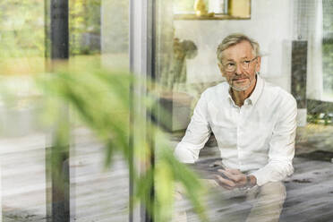 Senior man with grey hair in modern design living room with tablet sitting on couch - SBOF02086