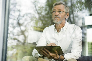 Älterer Mann mit grauen Haaren in modernem Design Wohnzimmer mit Tablet sitzen auf Couch - SBOF02088