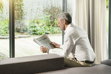 Senior man with grey hair in modern design living room reading newspaper - SBOF02090