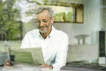 Älterer Mann mit grauen Haaren in modernem Design-Wohnzimmer beim Zeitungslesen - SBOF02093