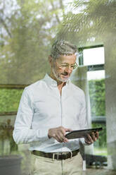 Lächelnder älterer Mann mit grauen Haaren in modernem Design-Wohnzimmer mit Tablet - SBOF02097
