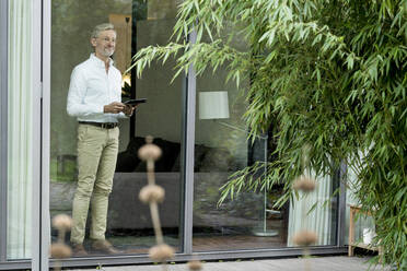 Senior Mann mit grauen Haaren in modernem Design Wohnzimmer hält Tablet - SBOF02100