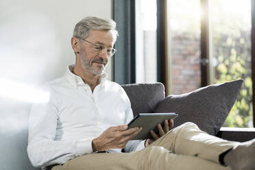 Älterer Mann mit grauen Haaren in modernem Design Wohnzimmer sitzen auf Couch mit Tablet - SBOF02105