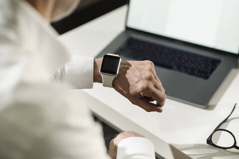 Nahaufnahme der Hand eines älteren Mannes mit Smartwatch und Laptop, lizenzfreies Stockfoto