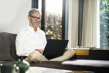 Senior man with grey hair in modern design living room working on laptop in home office - SBOF02123