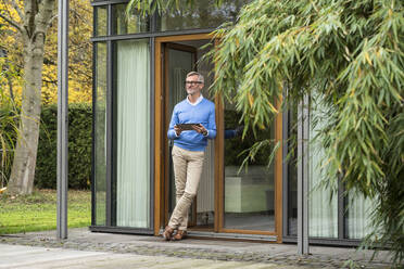 Älterer Mann mit grauen Haaren steht vor seinem modernen Designhaus und hält ein Tablet in der Hand - SBOF02128