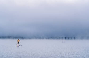 Man stand up paddle surfing on a lake in the fog - DGOF00456