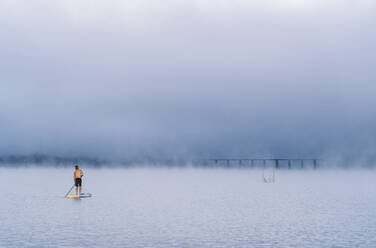 Mann beim Stand Up Paddle Surfing auf einem See im Nebel - DGOF00456