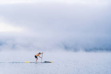 Mann beim Stand Up Paddle Surfing auf einem See im Nebel - DGOF00458