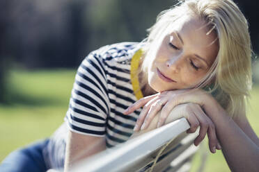 Blonde lächelnde Frau sitzt auf einer Bank und schaut in die Kamera - JSMF01438
