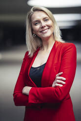 Blond smiling businesswoman with arms crossed wearing red suit and looking at camera - JSMF01450